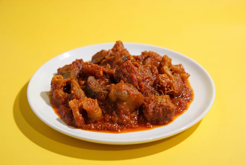 A white plate filled with a rich, reddish-brown stew against a bright yellow background.