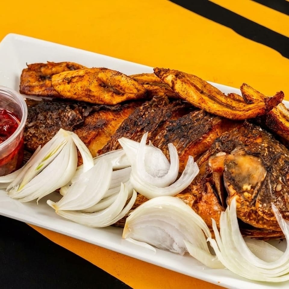Grilled whole fish with plantains, sliced onions, and a side of red pepper sauce.